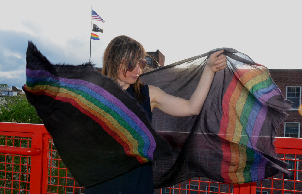 Empar unfurls our Diversity Pride shawl. In the background the Pride Flag flies above City Hall, Ithaca NY